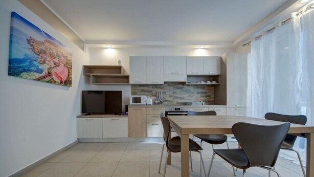 A modern kitchen with white cabinets, a tiled backsplash, and a dining area with a wooden table and chairs. - Modern 3BR home with Balcony in Central Msida (L-Imsida)