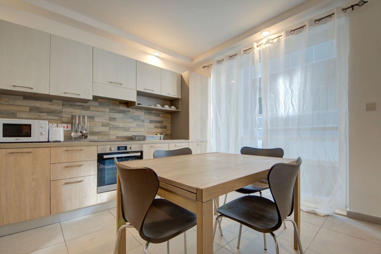 Una cucina moderna con tavolo e sedie, forno a microonde, forno e rivestimento a piastrelle.
