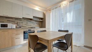 A modern kitchen with a dining table and chairs, a microwave, oven, and a tiled backsplash. - Modern 3BR home with Balcony in Central Msida (L-Imsida)
