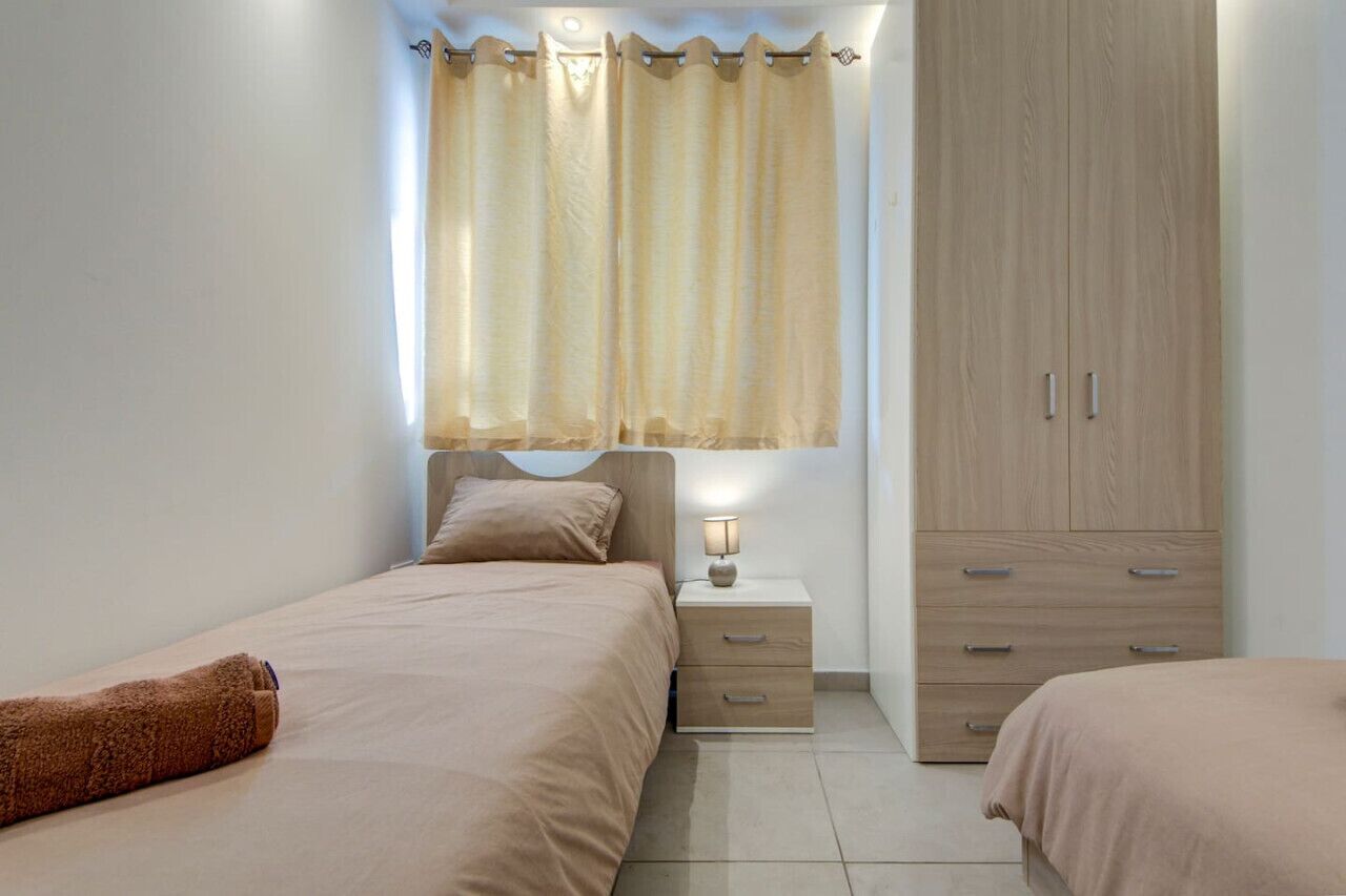 Una camera da letto con due letti, un comodino con una lampada, un armadio e una finestra con tende.