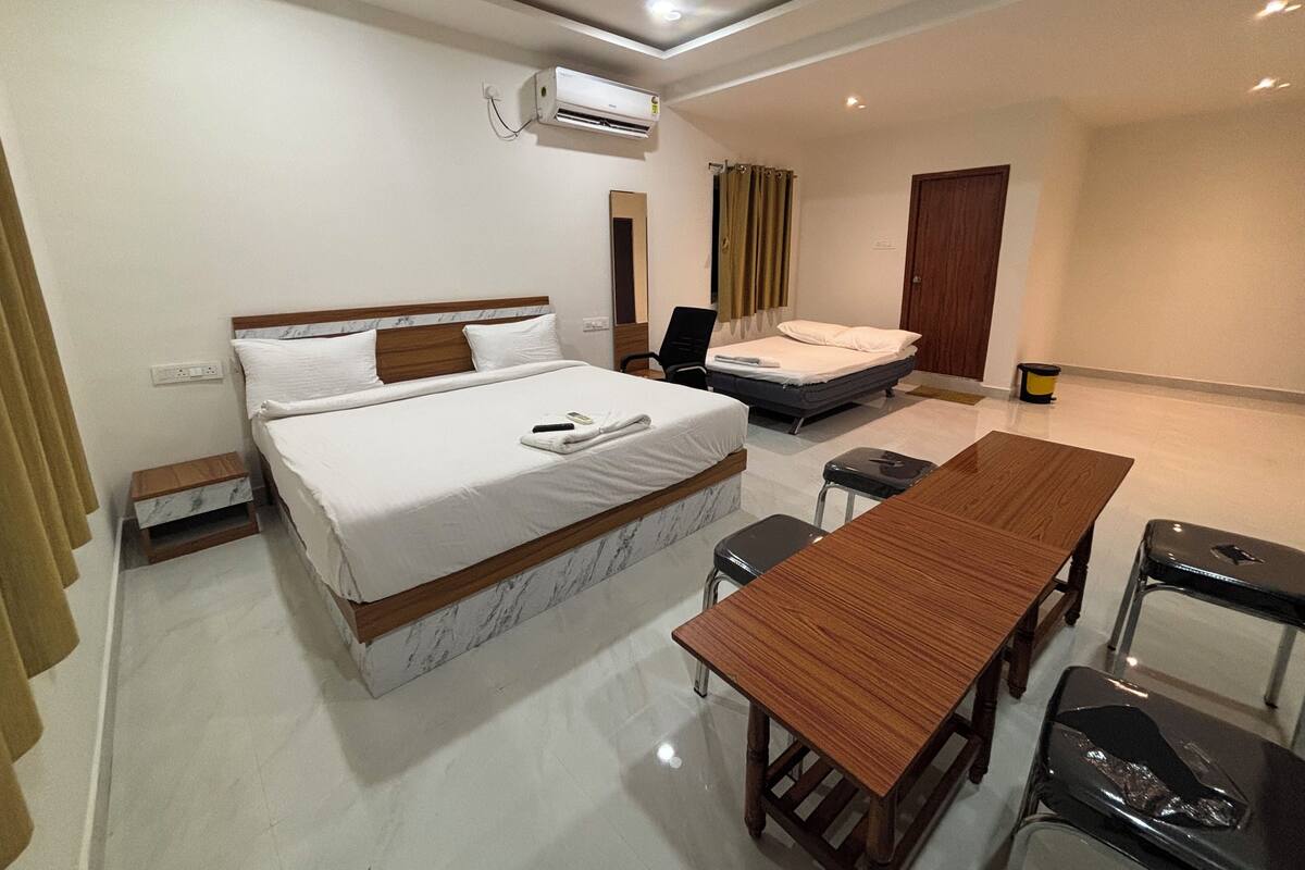Une chambre d’hôtel avec un grand lit, un bureau et une chaise. Il y a une fenêtre avec des rideaux, un appareil de climatisation et une porte.