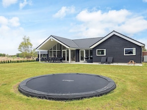 A residential house with a covered patio, a trampoline in the yard, and a clear sky.