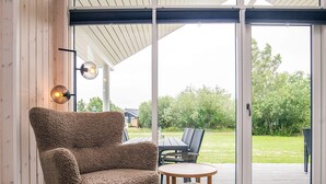 Ein gemütliches Zimmer mit einem großen Fenster, einem bequemen Ohrensessel, einem kleinen runden Tisch und passendem Hocker.