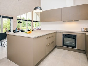 A modern kitchen with a large island, built-in oven, and ample natural light from large windows.