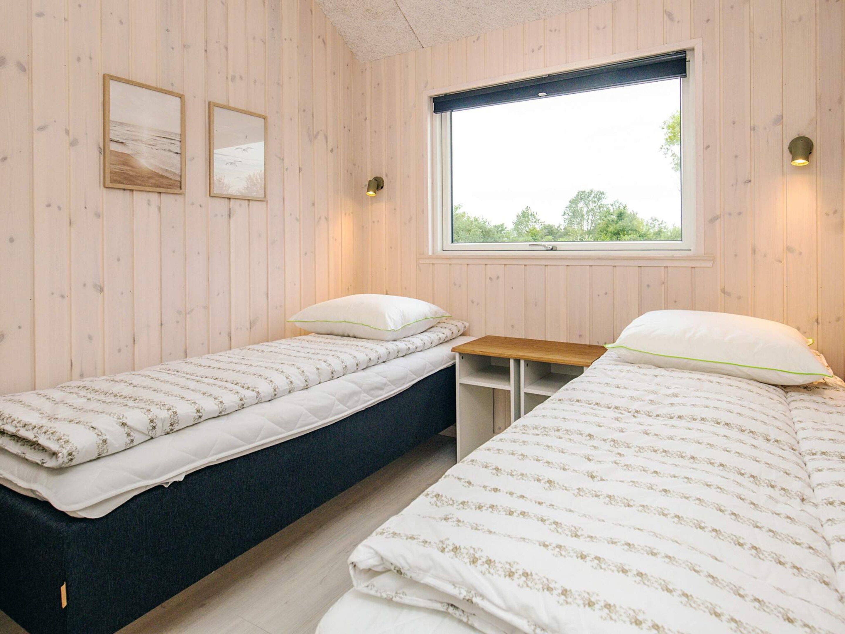 Een kamer met twee bedden, een raam en twee aan de muur bevestigde fotolijstjes.