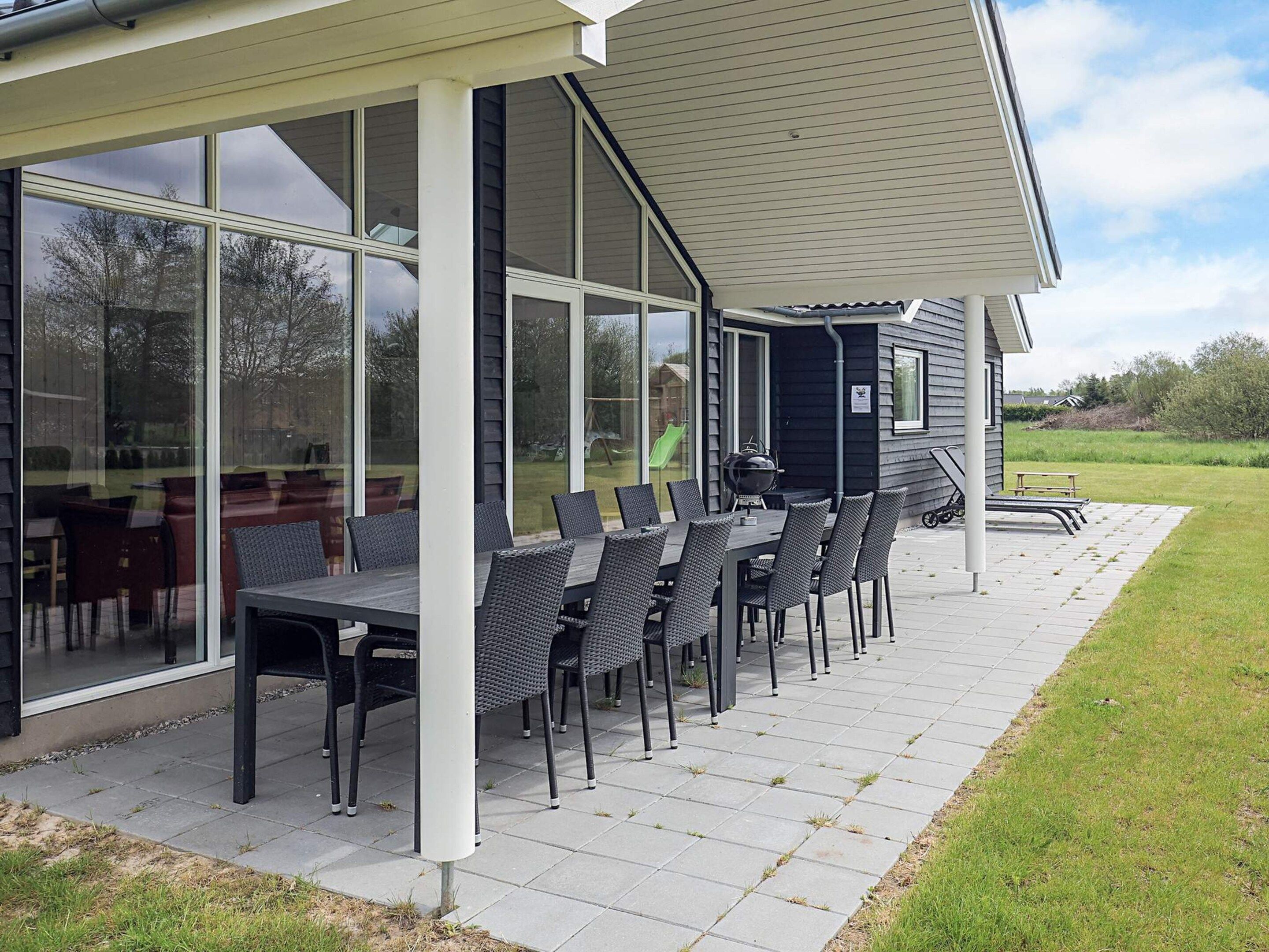 Een buitenpatio met een tafel, stoelen, een barbecue en een overdekt gedeelte met grote ramen.