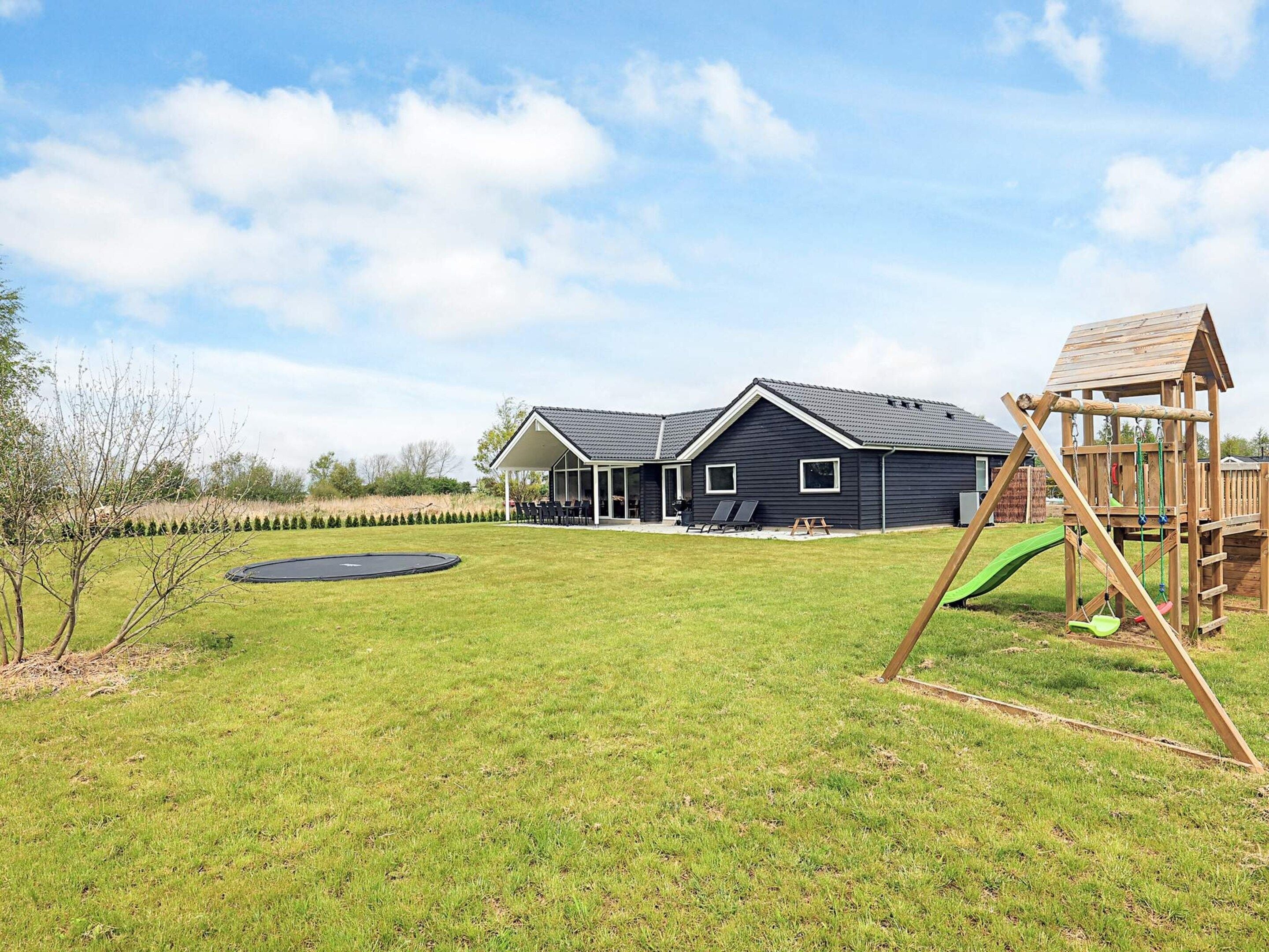 A backyard with a trampoline, a wooden playhouse, and a house with a covered patio.