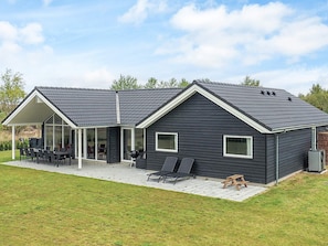 Et moderne hus med en overdækket terrasse, græsplæne og et stort vindue.