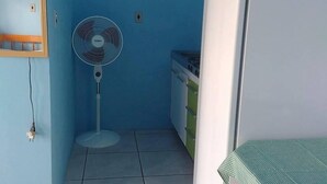 A small room with a blue wall, a standing fan, a white refrigerator, and a green tablecloth-covered table. - Pousada Água Azul (Capao da Canoa)