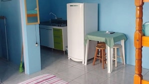 A small, compact room with a kitchenette, a single bed, a television mounted on the wall, and a wooden chair. - Pousada Água Azul (Capao da Canoa)