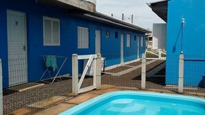 A blue building with a pool, a gate, and a staircase leading to a balcony. - Pousada Água Azul (Capao da Canoa)