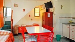 Habitación compacta con mesa y sillas, un pequeño rincón de cocina y una escalera que sube a otro nivel.