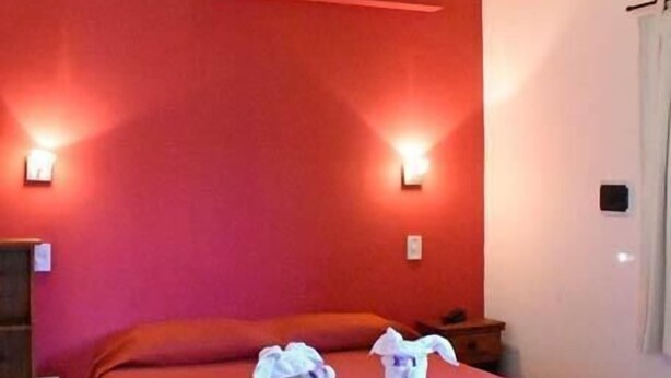 Habitación de hotel con dos camas, paredes rojas y techo de madera. Incluye luces fijadas a la pared y un equipo de aire acondicionado.