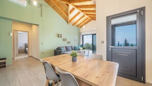 A spacious room with a wooden dining table, grey chairs, a grey sofa, and a large window with a view.