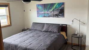Een slaapkamer met een bed, een plafondventilator, een nachtkastje, een lamp en een schilderij van het noorderlicht.