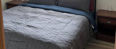 Une chambre à coucher comprenant un lit, une table de chevet, une commode, un ventilateur de plafond et une fenêtre donnant sur l’extérieur.