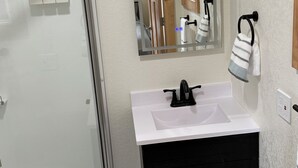 Een badkamer met een douchecabine van glas, een witte wastafel met een zwarte kraan en een spiegel erboven.