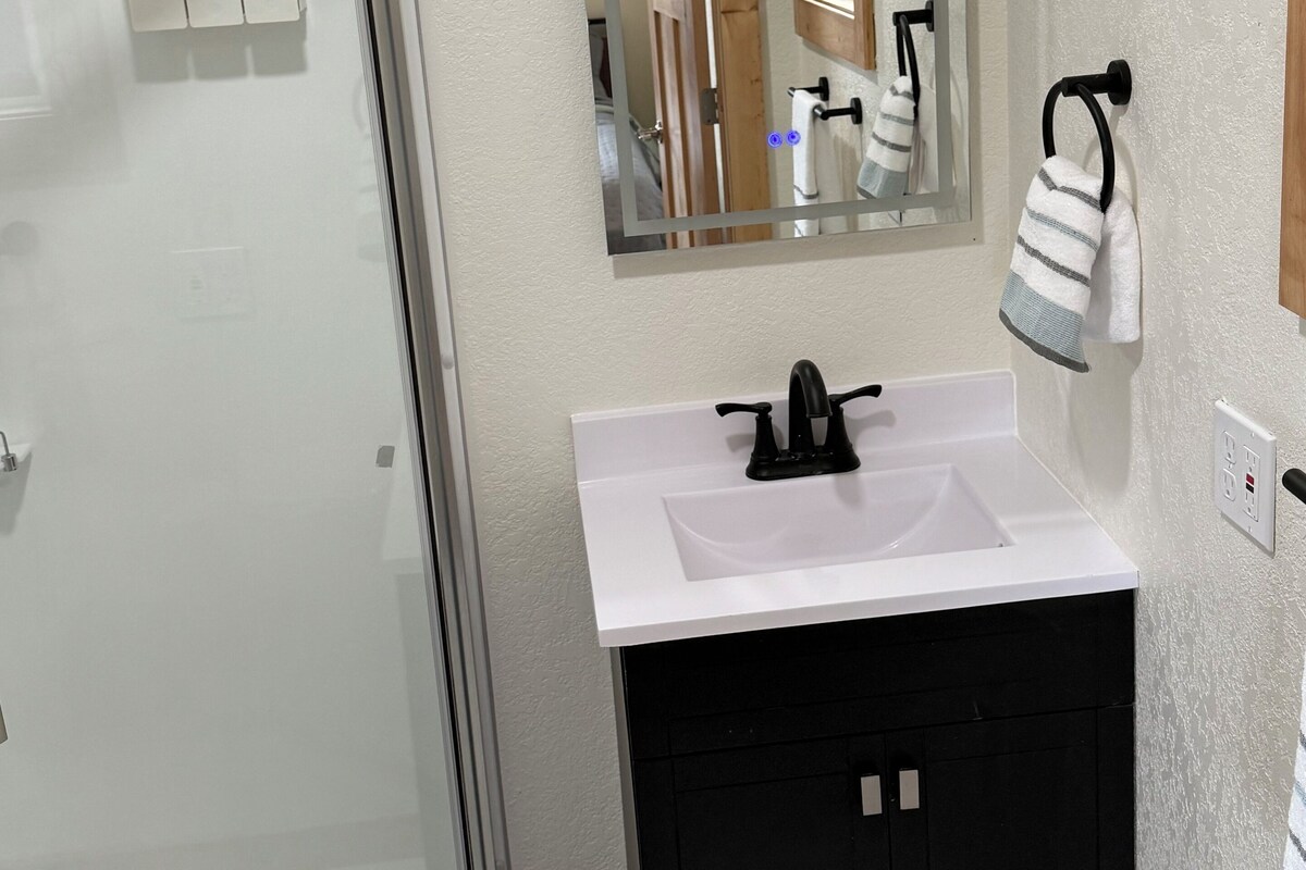 A bathroom with a glass shower enclosure, a white sink with a black faucet, and a mirror above the sink.