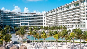 Un hotel de varios pisos, con piscina, sillas de descanso y palmeras.