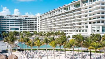 A hotel with multiple floors, a pool area with lounge chairs, and palm trees.