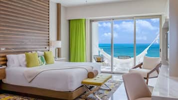 A hotel room with a large bed, a desk, a chair, and a view of the ocean through a sliding door.