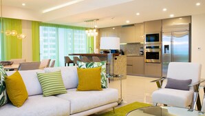 Una sala de estar moderna con sofá, sillones, comedor y cocina equipada.