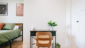 Une chambre à coucher avec un lit, un bureau, une chaise, une plante en pot et une poubelle.