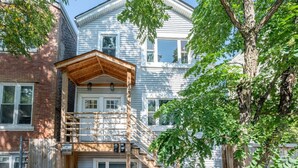 Une maison à deux étages dotée d’un porche couvert, d’un escalier en bois et d’un mur en briques qui lui est adjacent.