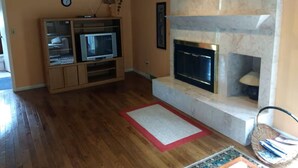 Ein Wohnzimmer mit Kamin, Holzboden, Fernseher und einem roten Teppich.