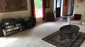 Ein Wohnzimmer mit großem Teppich, Couchtisch, Bücherregal und einer Tür zu einem weiteren Raum.