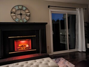 A living room with a fireplace, a large clock, and a sliding glass door leading to an outdoor area.