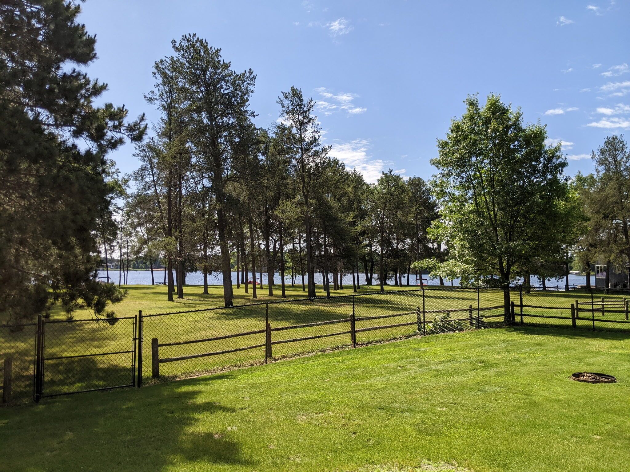 A fenced park area with a grassy field and trees, overlooking a body of water.