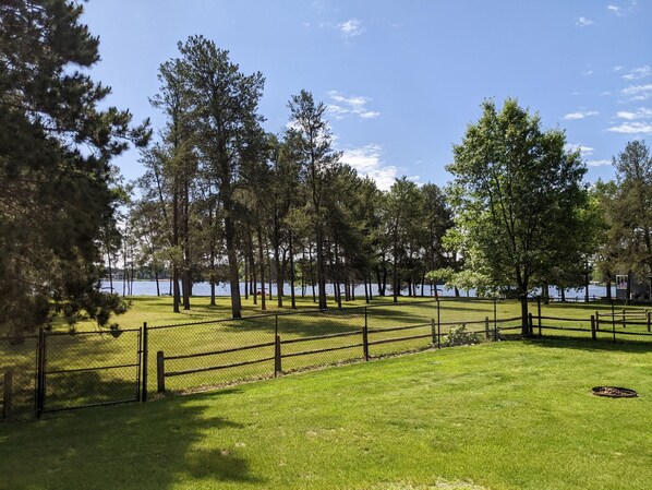 A fenced park area with a grassy field and trees, overlooking a body of water.