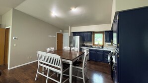 Una cocina amplia con armarios azul oscuro, un refrigerador de acero inoxidable y un comedor con mesa de madera y sillas blancas.