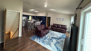 Un salón amplio con piso de madera oscura, un tapete de mármol azul, un sofá de cuero marrón y un comedor con una cocina al fondo.