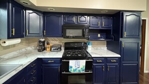 Una cocina con armarios azul oscuro, una estufa negra, un microondas y una encimera de mármol.