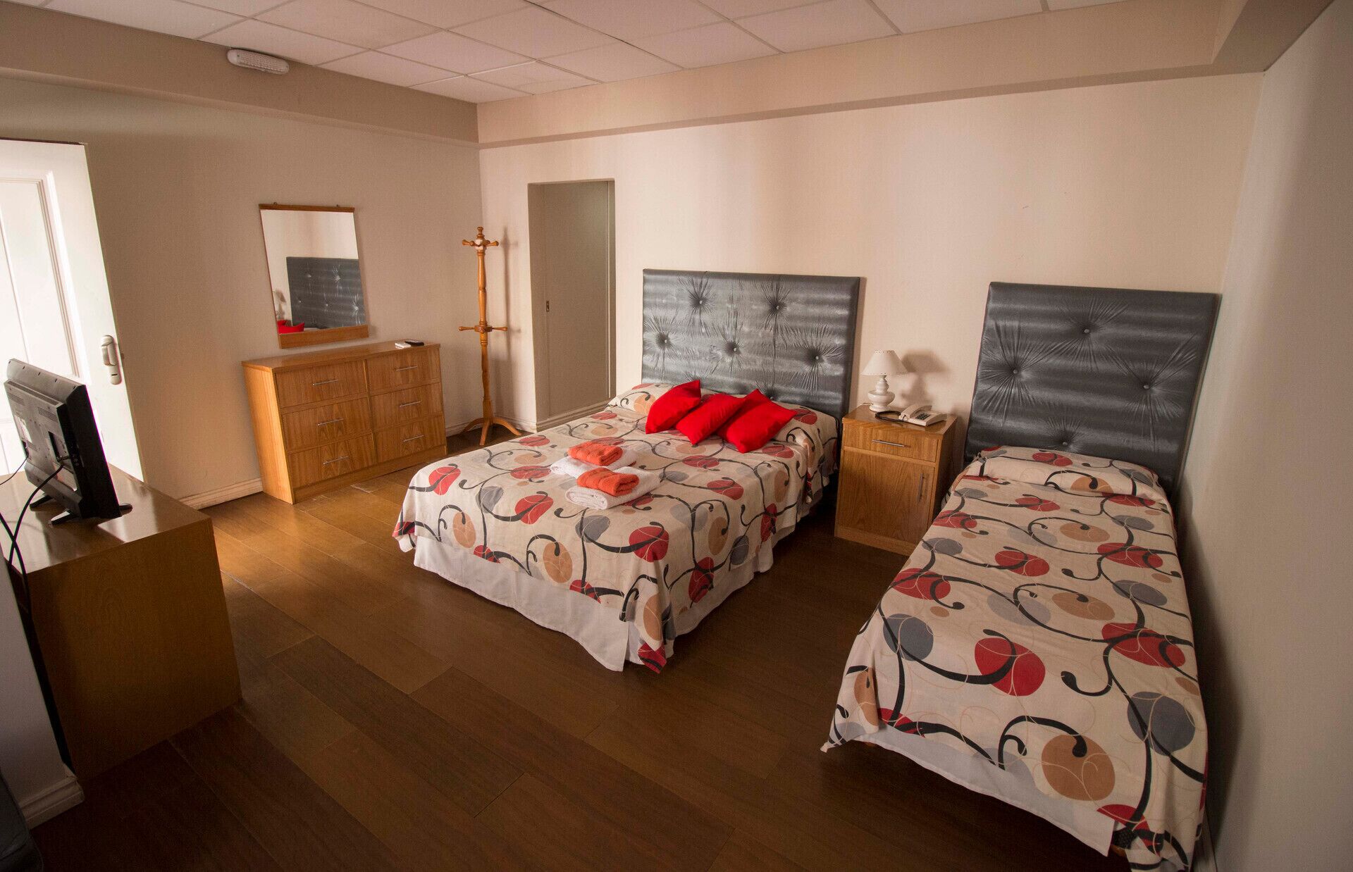 A bedroom with two beds, a wooden dresser, a mirror, and a desk with a computer.