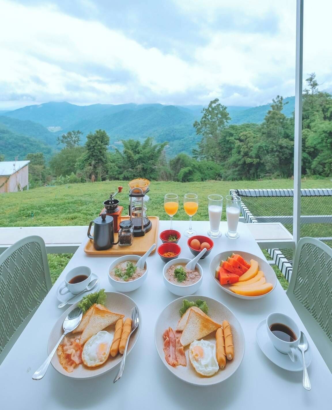 A breakfast table set with various dishes, including eggs, toast, and fruit, overlooking a scenic landscape.