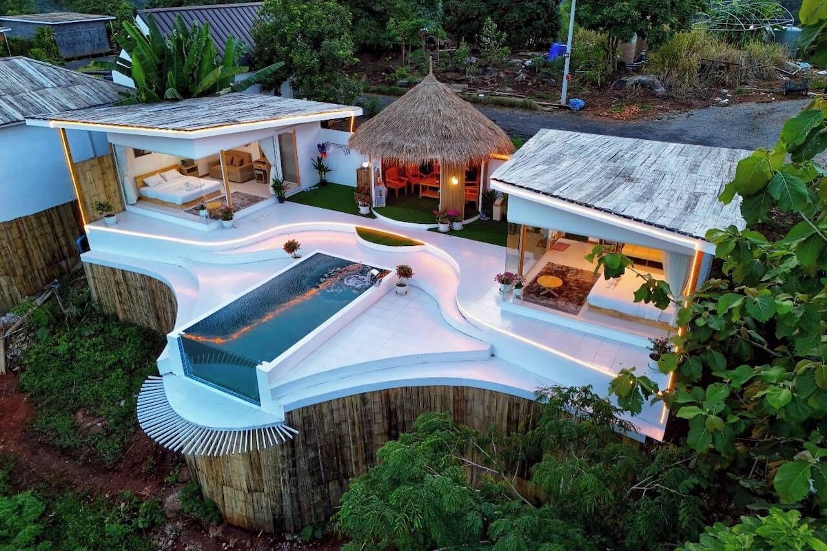 A modern villa with a pool, outdoor seating, and a thatched-roof structure.