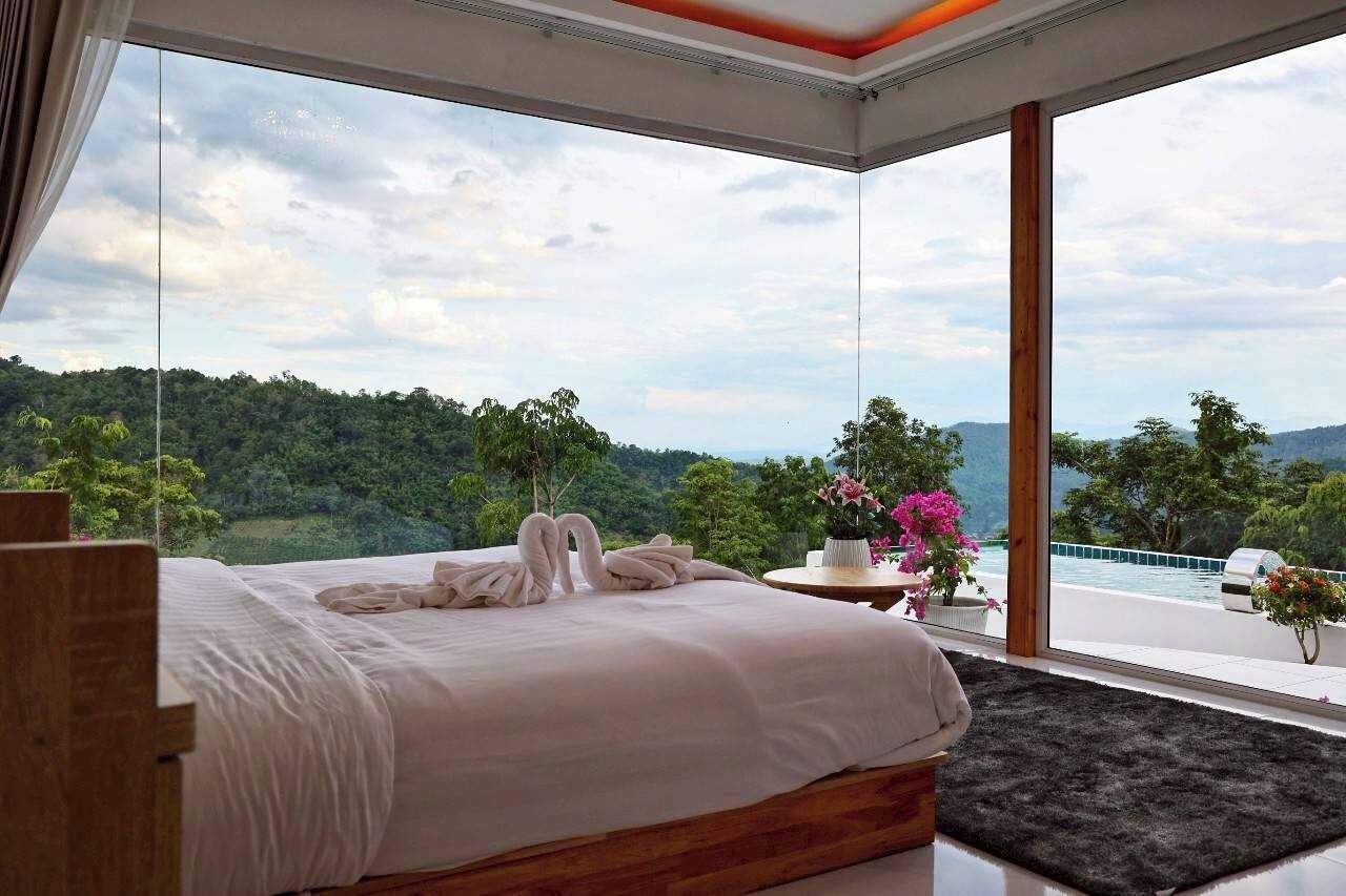 A bedroom with a large bed, a view of a mountainous landscape, and a small table with a vase of flowers.
