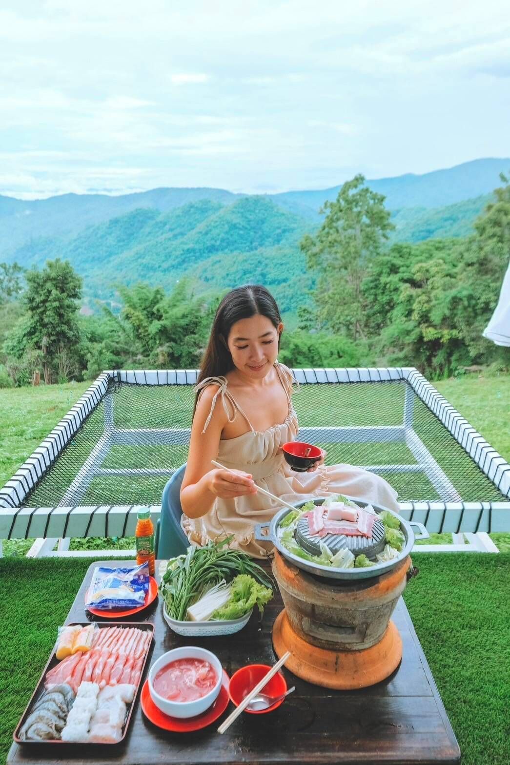 A person sitting at a table with a grill, various meats, vegetables, and condiments.
