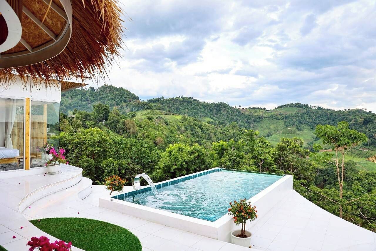 A private pool with a view of lush green hills, a thatched roof structure, and a white outdoor seating area.