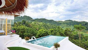 A private pool with a view of lush green hills, a thatched roof structure, and a white outdoor seating area.