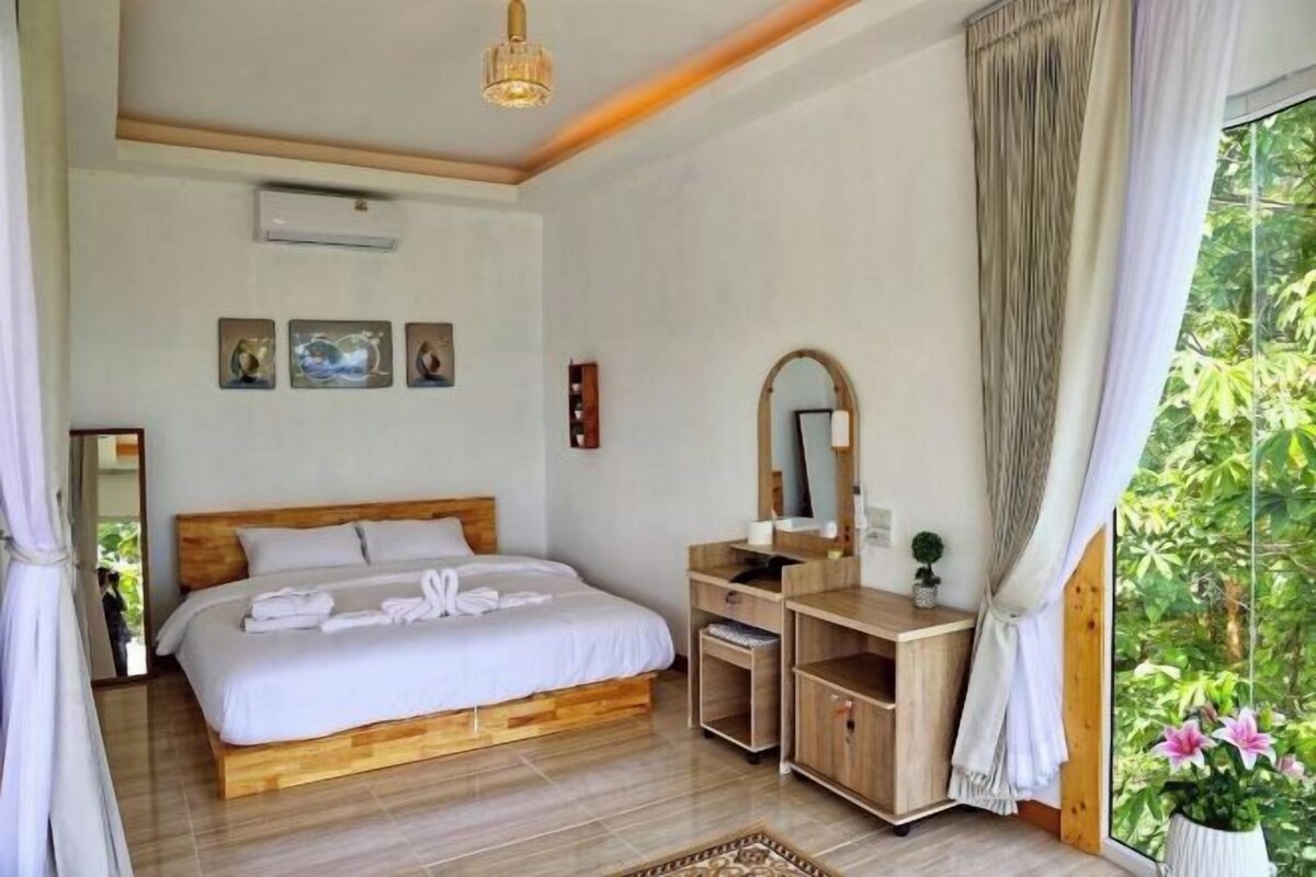 A bedroom with a wooden bed, a desk, a mirror, and a window with curtains.