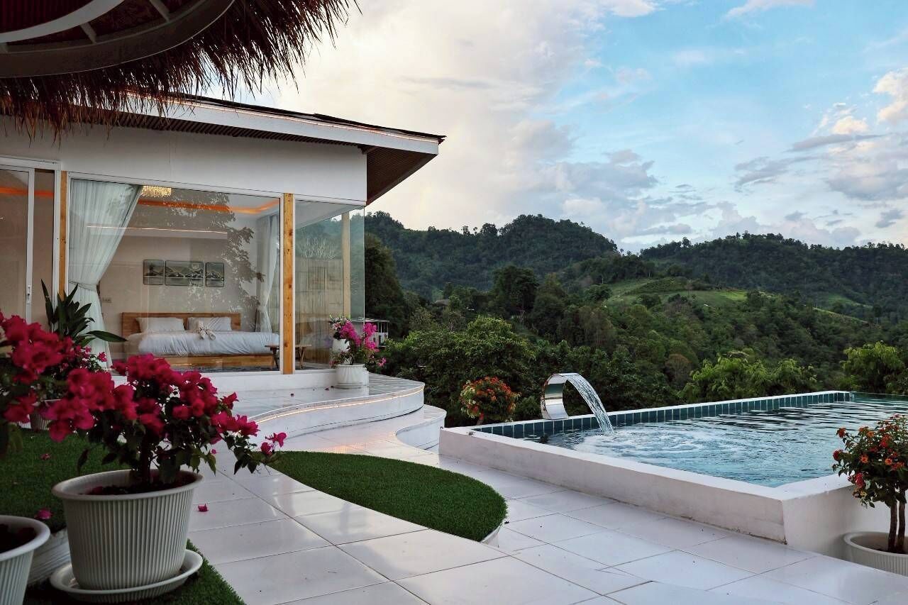 A modern villa with a private pool, a balcony with a sofa and a dining area, and a lush garden.