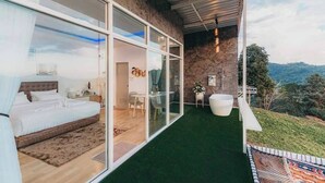 Un dormitorio moderno con una cama grande, un ventanal de vidrio a un balcón y vistas del paisaje circundante.