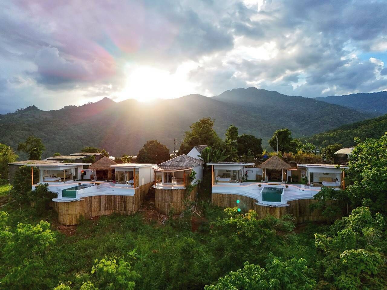 Un resort con varias cabañas tipo bungalow, cada una con piscina privada, frente a un paisaje de montañas y exuberante vegetación.