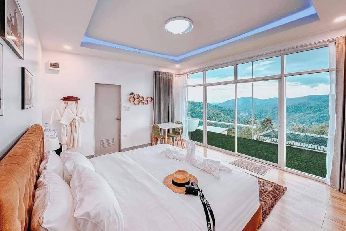 A hotel room with a large bed, a view of the mountains, and a balcony with a table and chairs.
