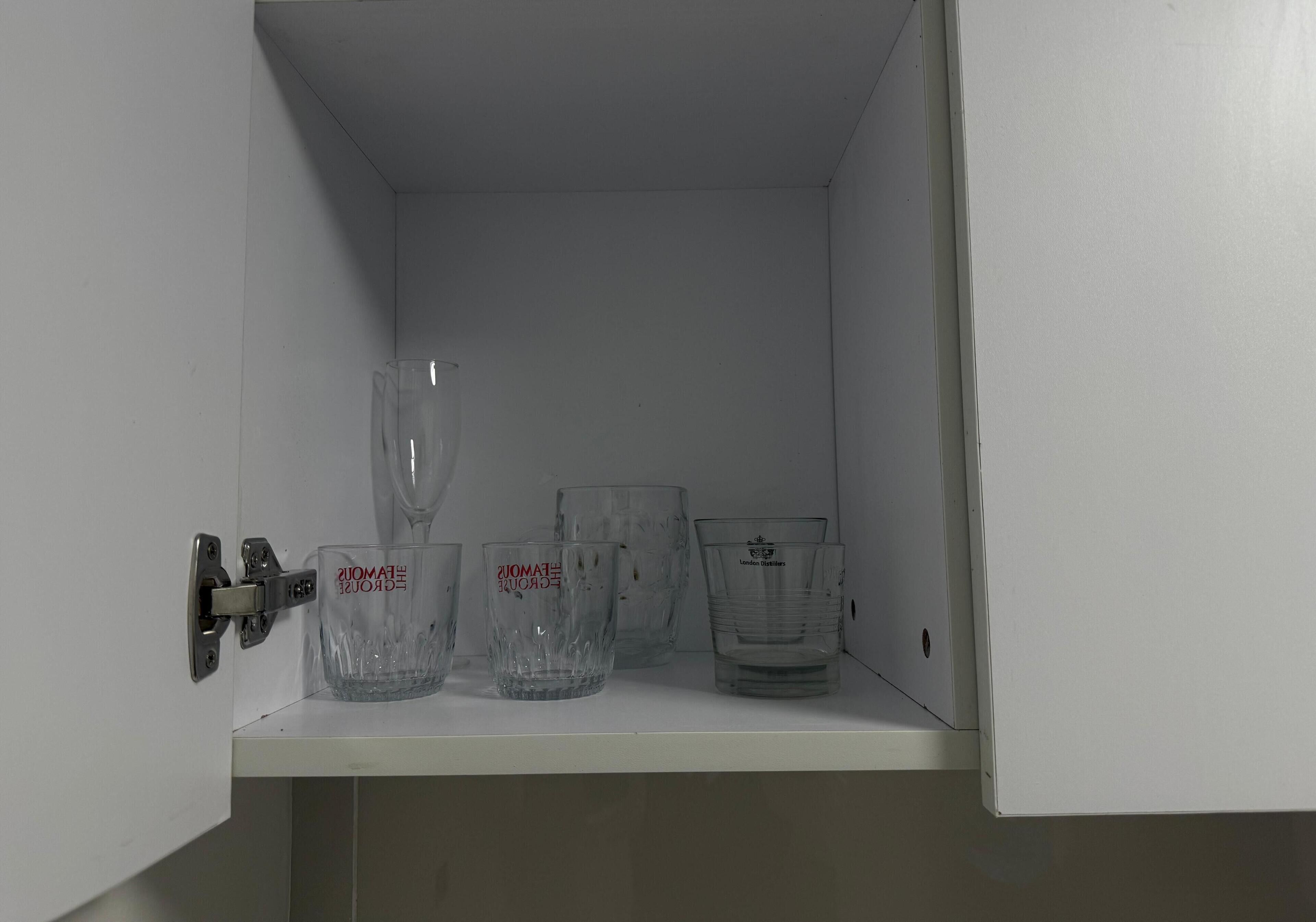 A white cabinet with a shelf containing three clear glass tumblers and a glass carafe.