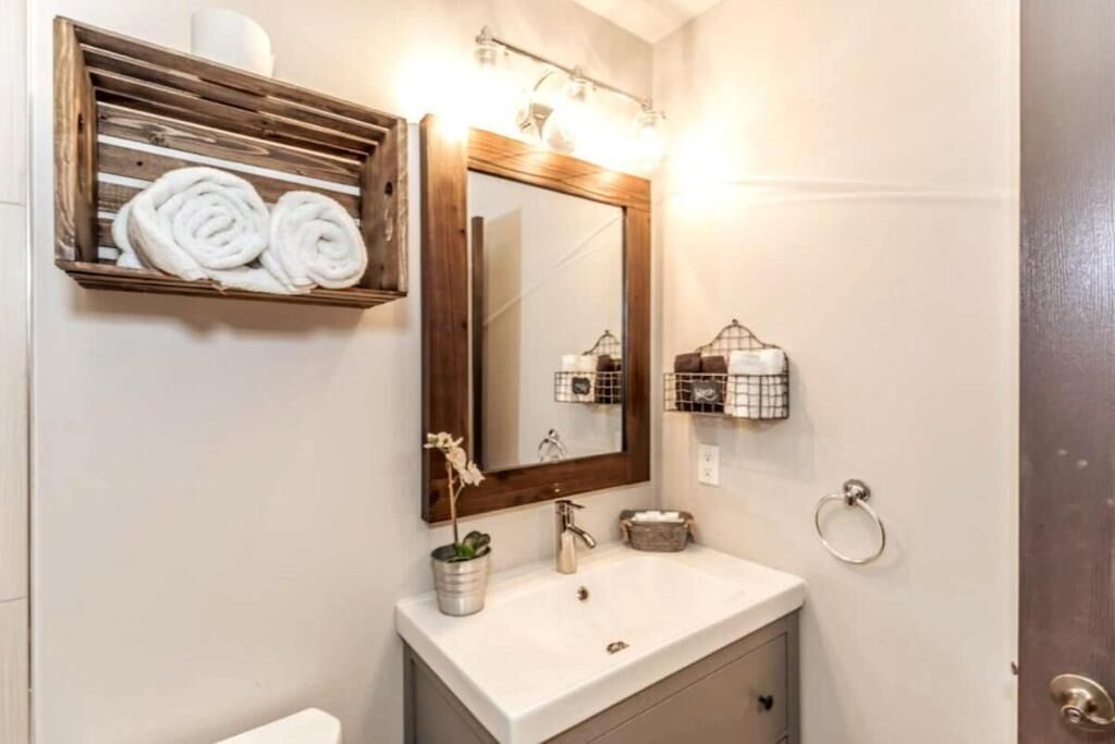 Une salle de bain avec un miroir encadré en bois, un lavabo blanc et un porte-serviettes avec des serviettes pliées.